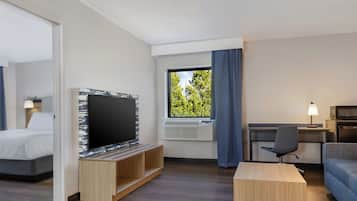 Habitación de hotel con cama, televisión, escritorio, silla y ventana con cortinas.