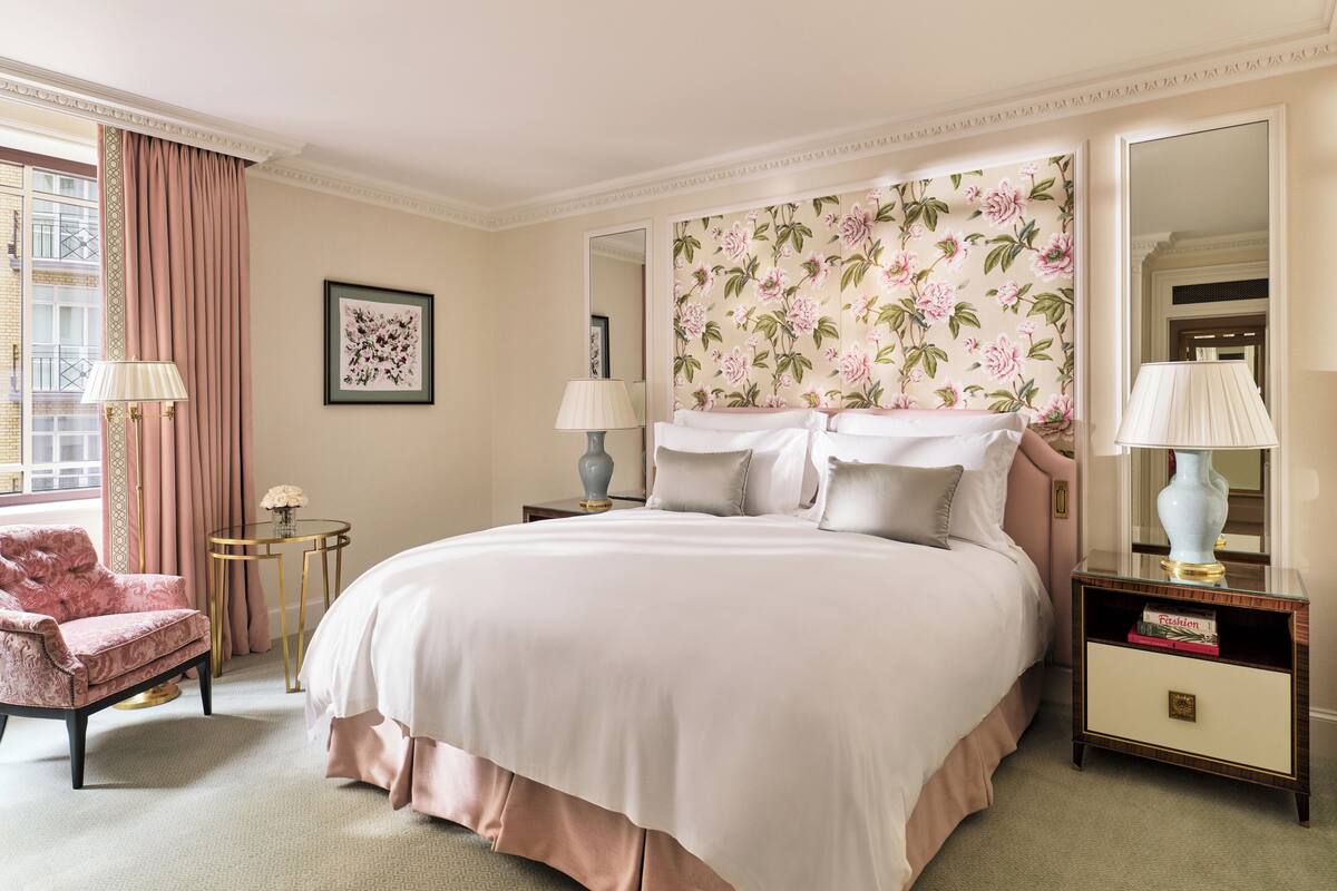 A hotel room with a large bed, two bedside tables, a chair, a mirror, and a window with curtains.