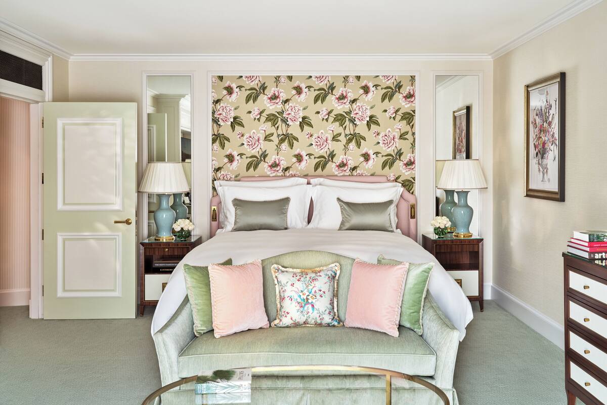 A bedroom with a floral wallpaper headboard, a green sofa, and two bedside tables with lamps.