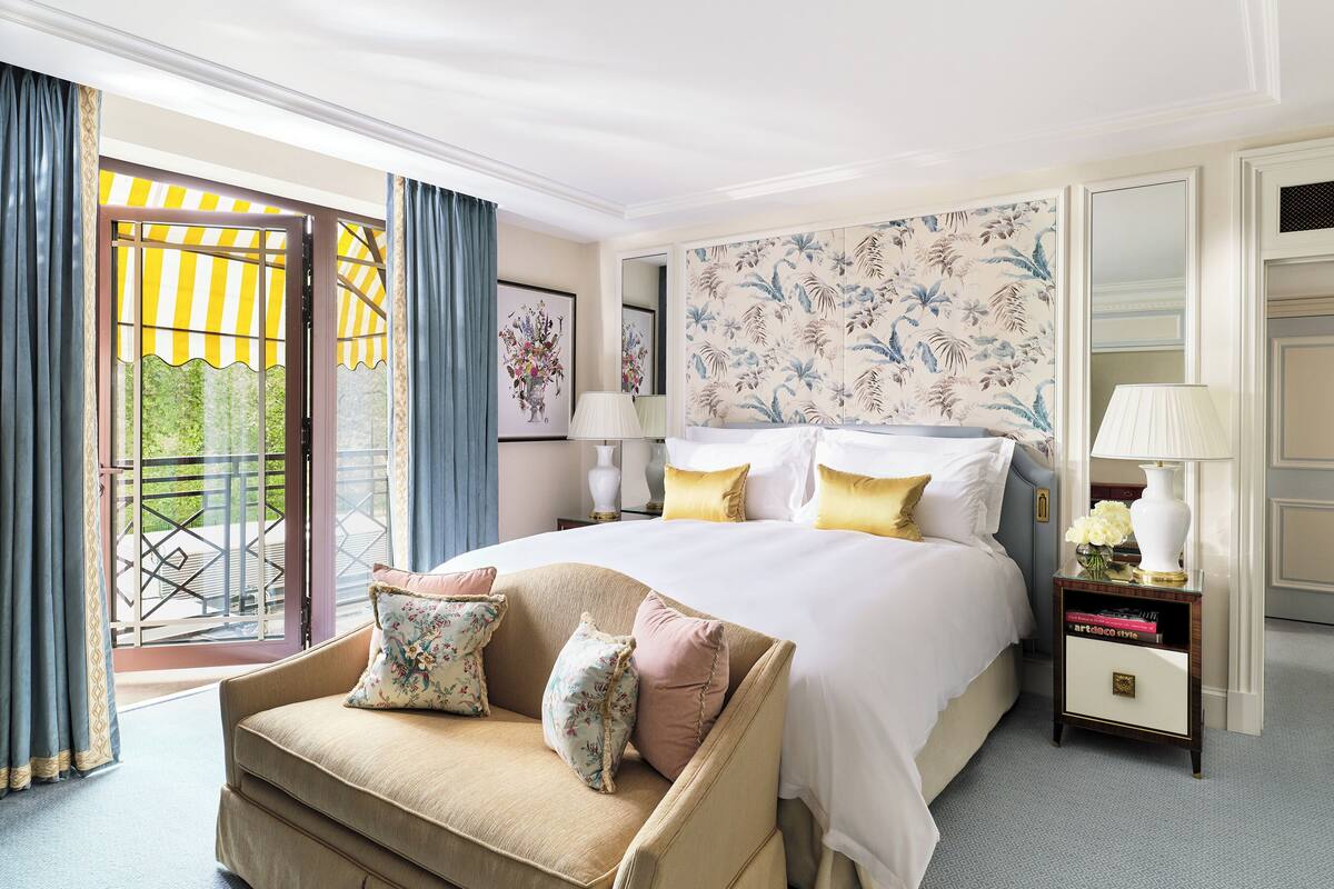 Una habitación de hotel con una cama grande, un sofá, una mesita de noche y un balcón con cortinas.