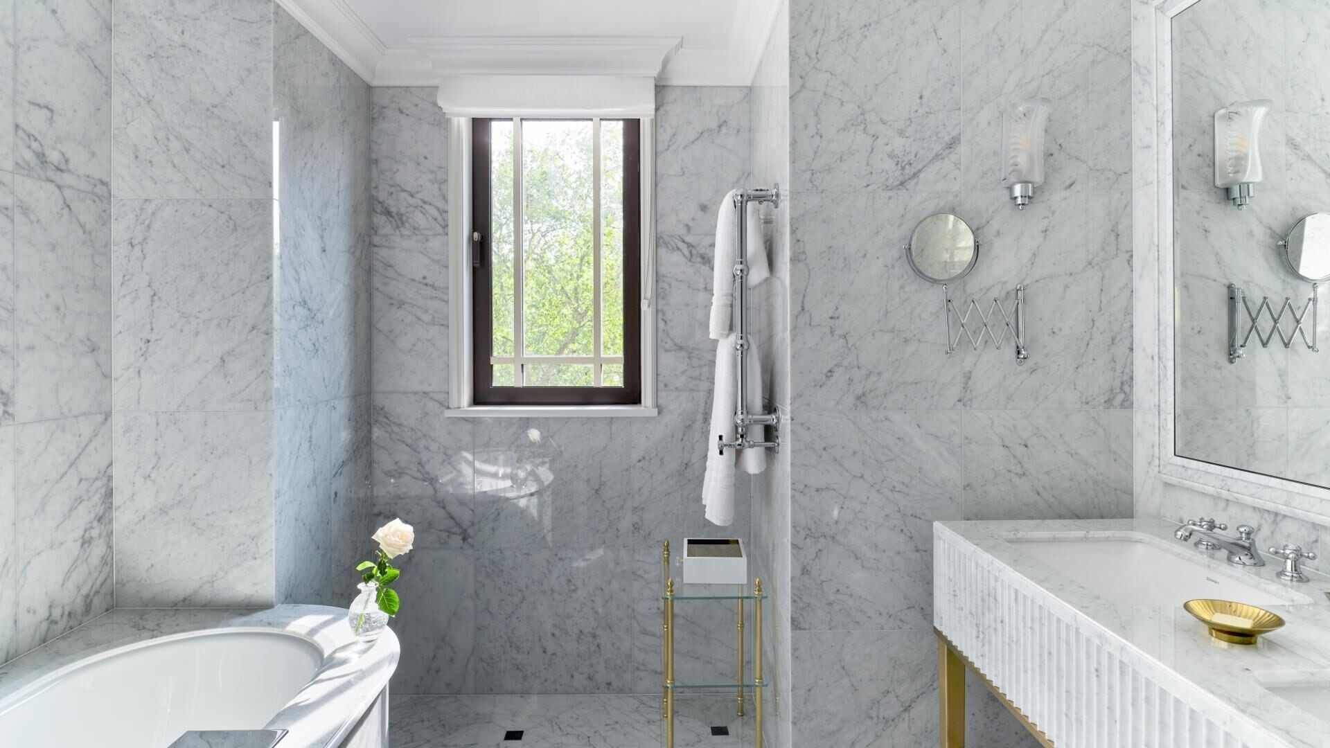 A modern bathroom with a bathtub, a glass shower enclosure, a vanity with a sink, and a window providing natural light.