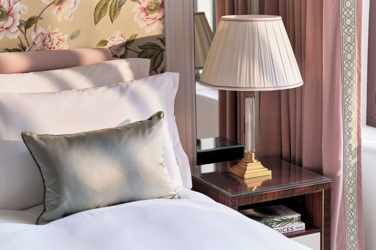 A neatly made bed with white linens, a green pillow, and a bedside table with a lamp and books.