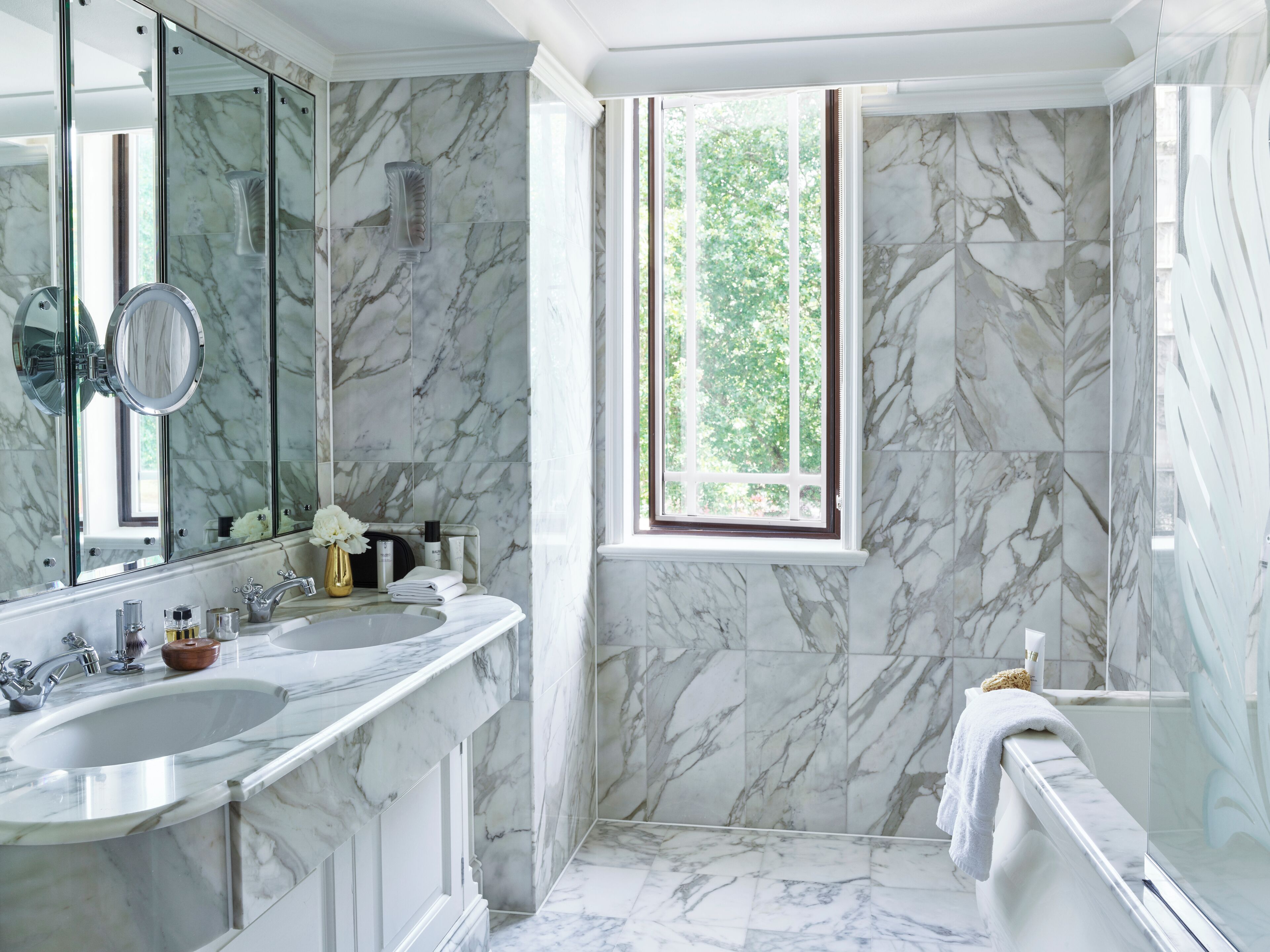 A bathroom with a marble sink, a large mirror, and a window providing a view of greenery.