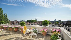 Una terraza en la azotea con plantas en macetas, una mesa y sillas.