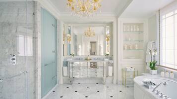 A luxurious bathroom with a marble floor, a large mirror, a chandelier, and a glass shower enclosure.