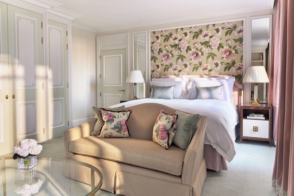 A bedroom with a bed, a sofa, a glass coffee table, a nightstand, and a mirror.