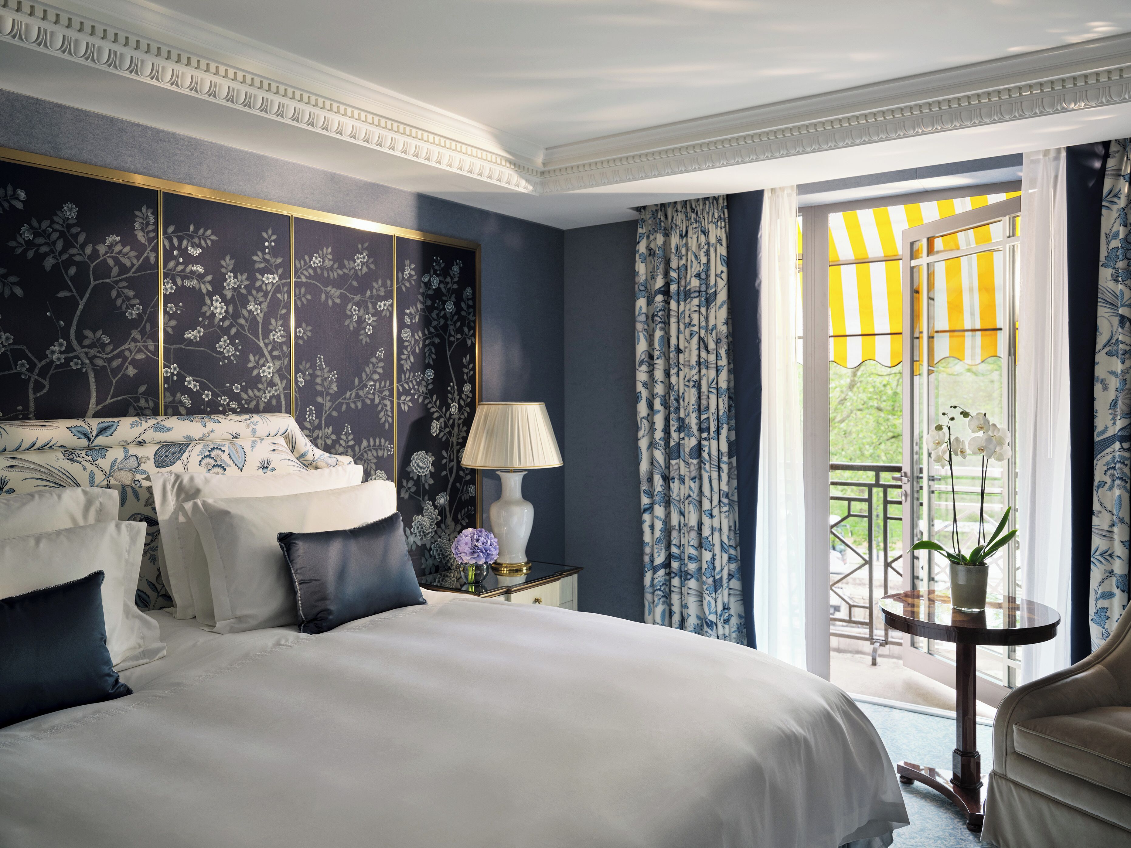 A bedroom with a bed, a nightstand, a lamp, a window with curtains, and a view of the outdoors.