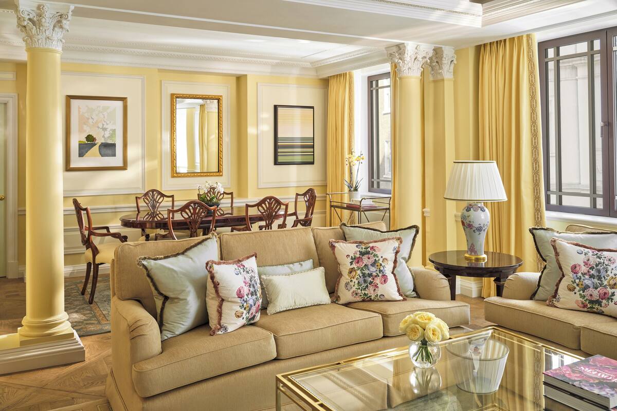 A well-appointed living room with a beige sofa, floral cushions, a glass coffee table, and a dining area with wooden chairs and a table.