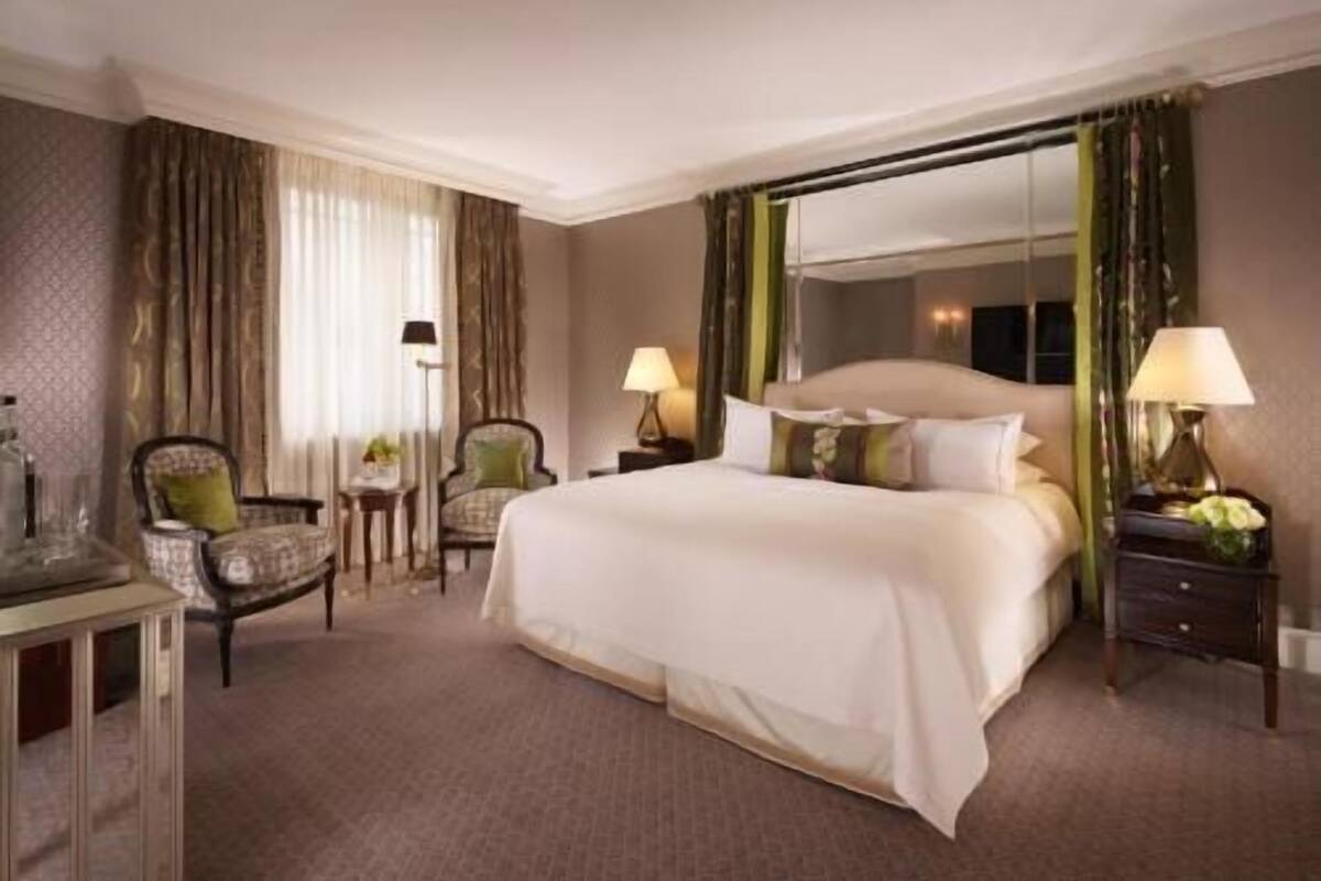 Una habitación de hotel con una cama grande, dos sillas, una mesita de noche y un espejo.