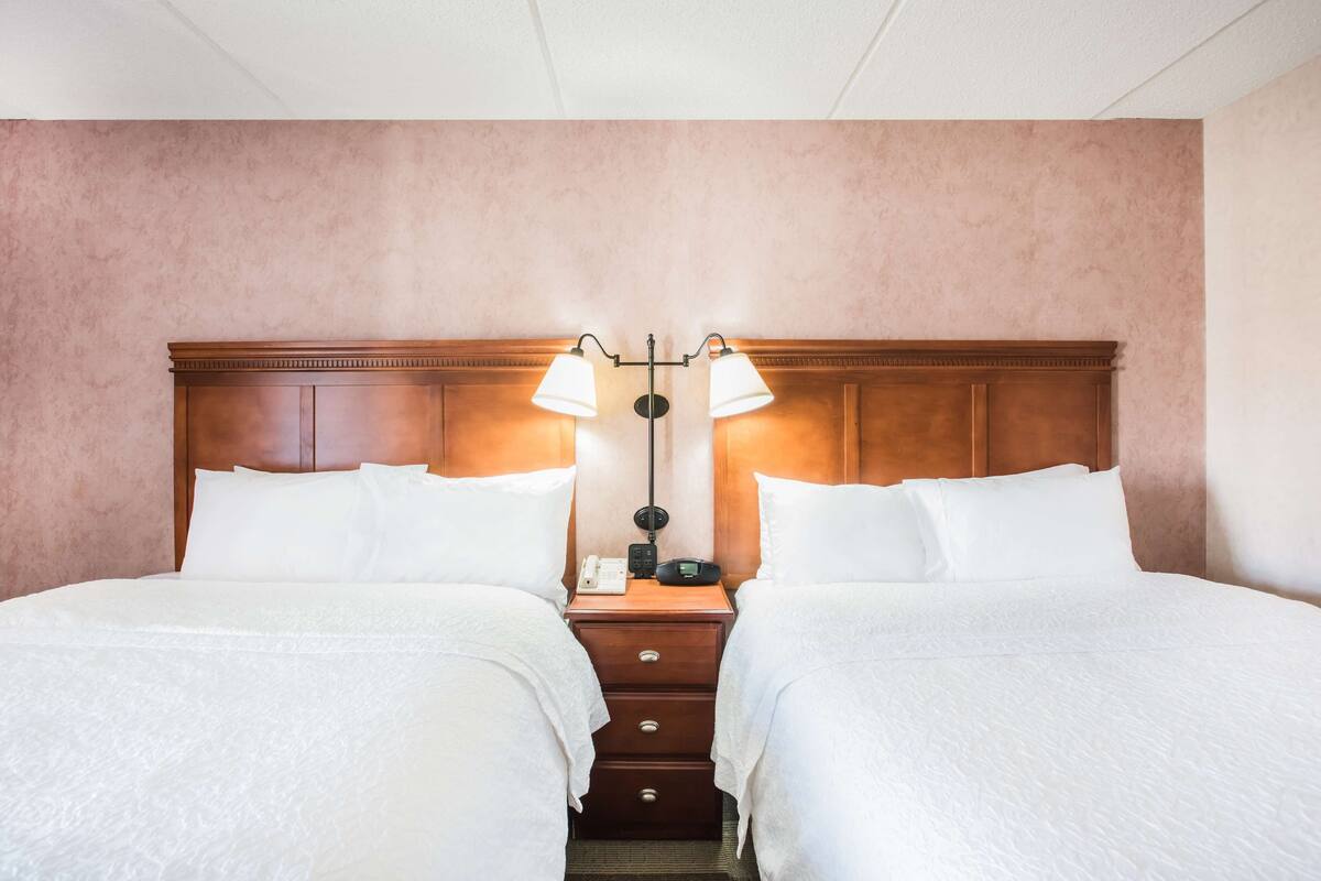 A hotel room with two beds, a wooden headboard, a nightstand with a lamp, and a telephone.