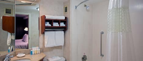 Un baño con lavamanos, inodoro y ducha. Hay un espejo, un perchero para toallas y una estantería con toallas.