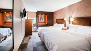 A hotel room with two beds, a desk, a TV mounted on the wall, and a view of the outdoors. - Hampton Inn West Springfield (West Springfield)