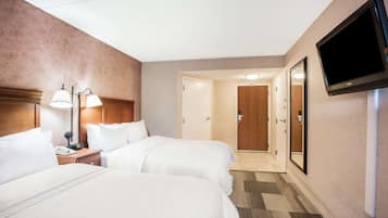 Habitación de hotel con dos camas, un escritorio con lámpara, un televisor montado en la pared y una puerta que da a un pasillo.