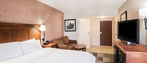 Habitación de hotel con una cama grande, un sofá, una mesita, un televisor y una puerta que da a otra habitación.