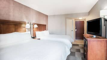 Una habitación de hotel con dos camas grandes, un televisor y un escritorio con lámpara.