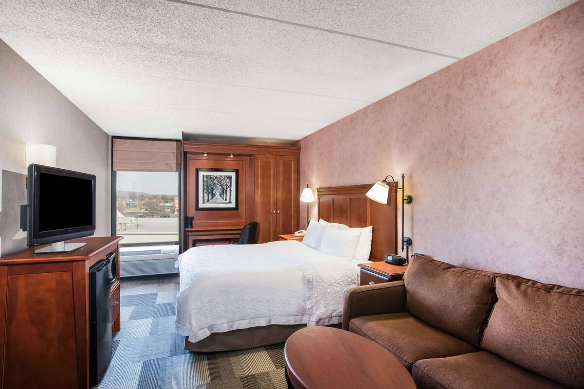 A hotel room with a bed, a television, a desk, a chair, a sofa, and a window with a view.