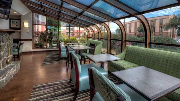 A restaurant with a glass-enclosed patio, wooden flooring, and green upholstered seating. - Hampton Inn West Springfield (West Springfield)