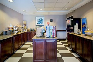 A hotel kitchen with a checkered floor, wooden cabinets, a central island, and various food and beverage dispensers.