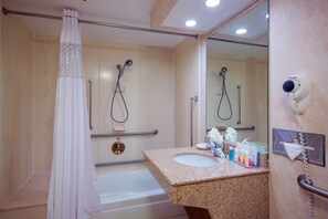 A bathroom with a shower, a sink with toiletries, a mirror, and a hairdryer mounted on the wall.