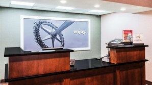 A reception desk with a large screen displaying a bicycle wheel and the word "enjoy." - Hampton Inn West Springfield (West Springfield)