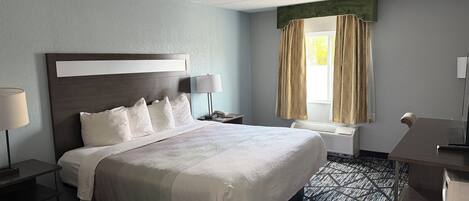A hotel room with a large bed, a desk, a chair, a lamp, and a window with curtains.