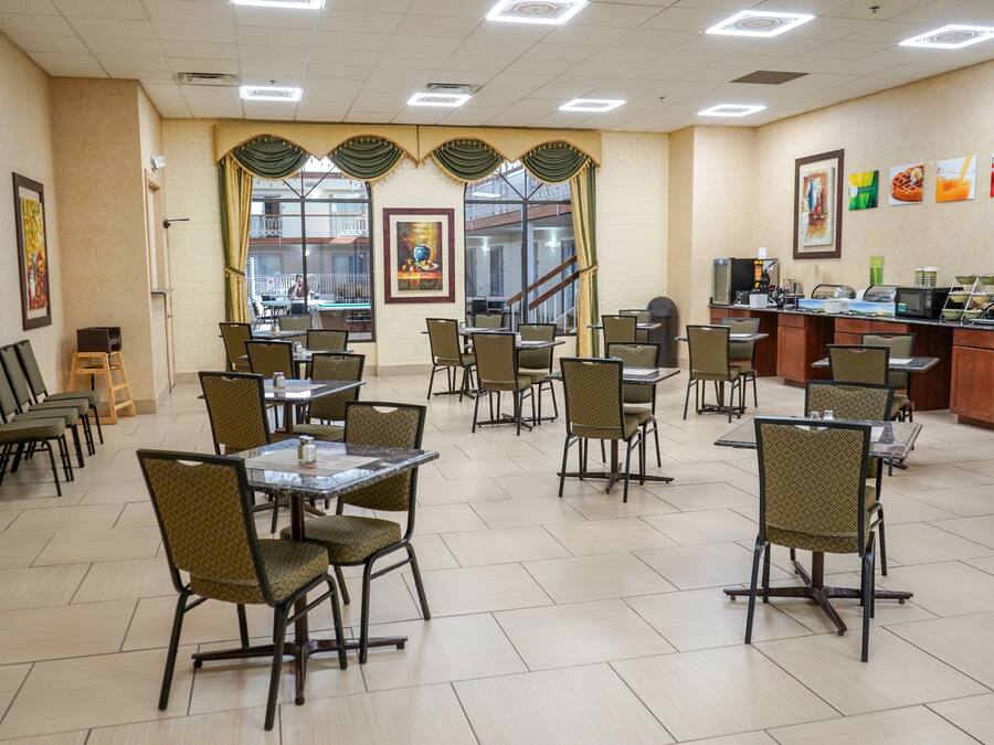 A spacious dining area with multiple tables and chairs, a buffet counter, and large windows with curtains.