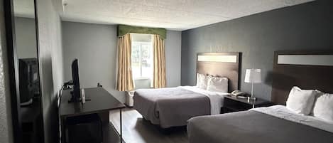 Habitación de hotel con dos camas, un escritorio, una silla, un televisor y una ventana con cortinas.