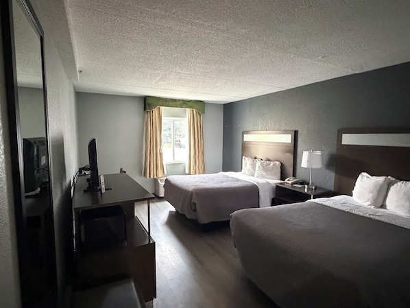 A hotel room with two beds, a desk, a chair, a TV, and a window with curtains.