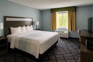 Une chambre d’hôtel avec un grand lit, des lampes de chevet, une fenêtre avec des rideaux, un bureau avec un téléviseur à écran plat et un climatiseur fixé au mur.