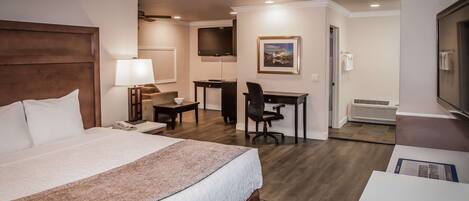 A hotel room with a large bed, a desk, a chair, a television, and a framed picture on the wall.