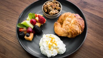 Un plato con un croissant, yogur y frutos rojos.