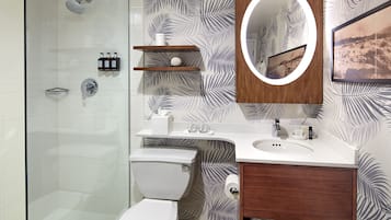 Un baño moderno con cabina de ducha de vidrio, inodoro, lavamanos con tocador de madera y espejo.