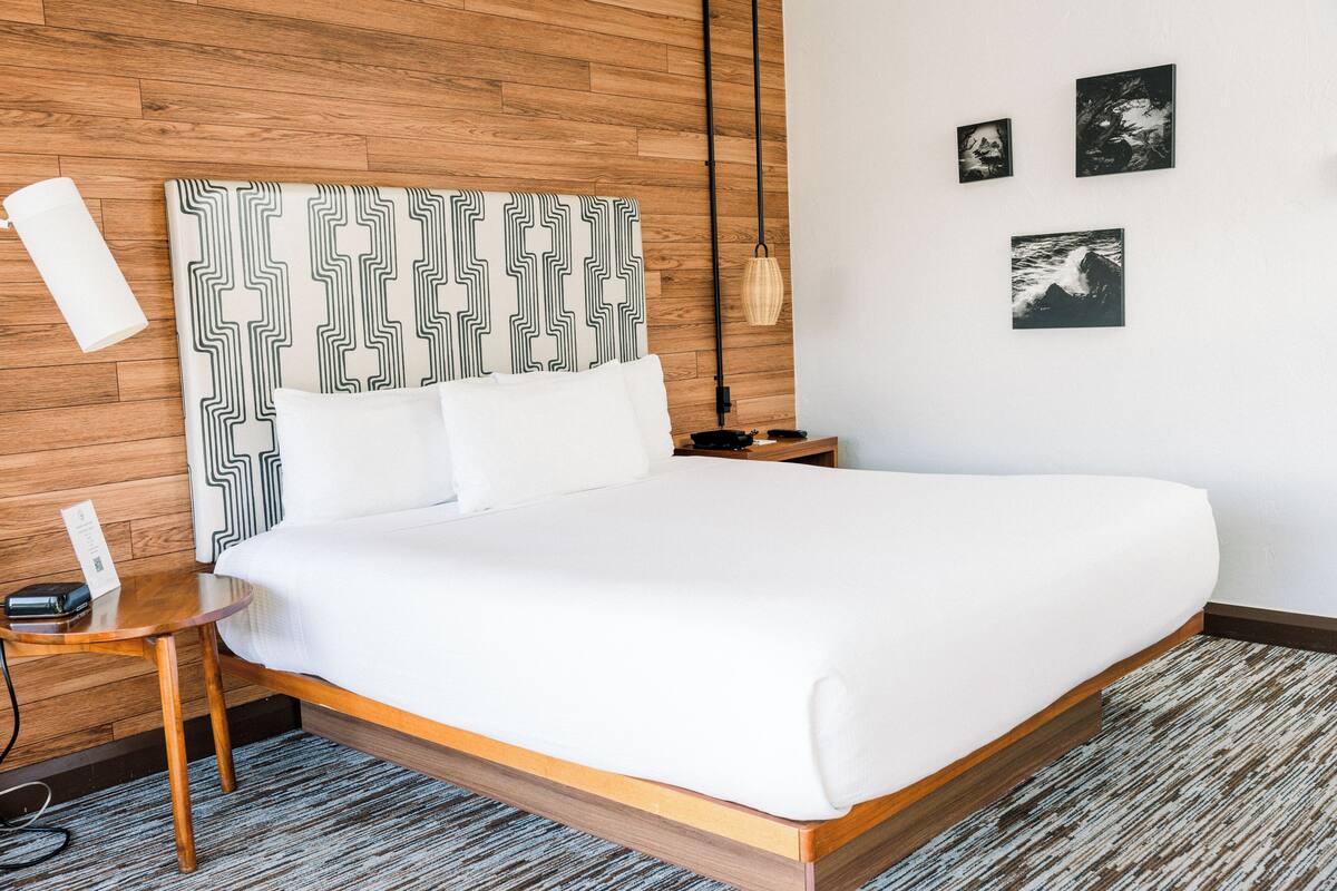 A neatly made bed with a patterned headboard, a bedside table with a lamp, and three framed pictures on the wall.
