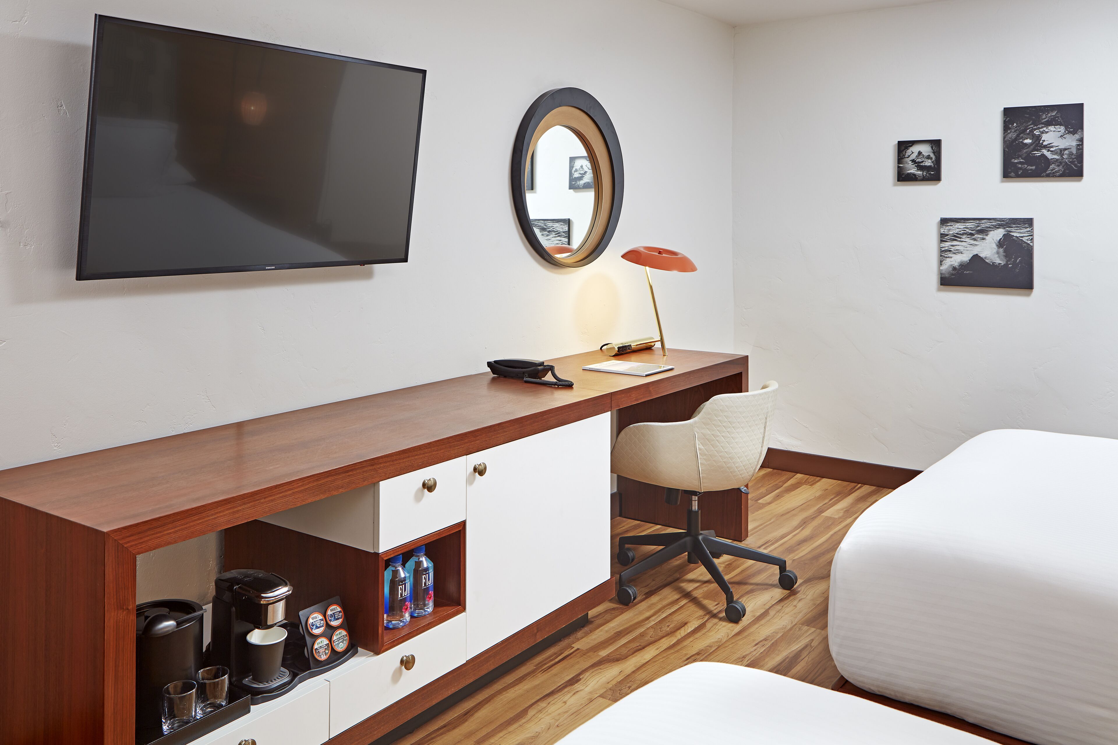 Ein Hotelzimmer mit einem Holztisch, einem Sessel, einem Bett, einem Fernseher, einem Spiegel und Bildern an der Wand.