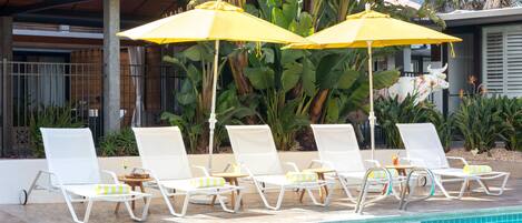 A poolside area with white lounge chairs and yellow umbrellas, surrounded by lush greenery.
