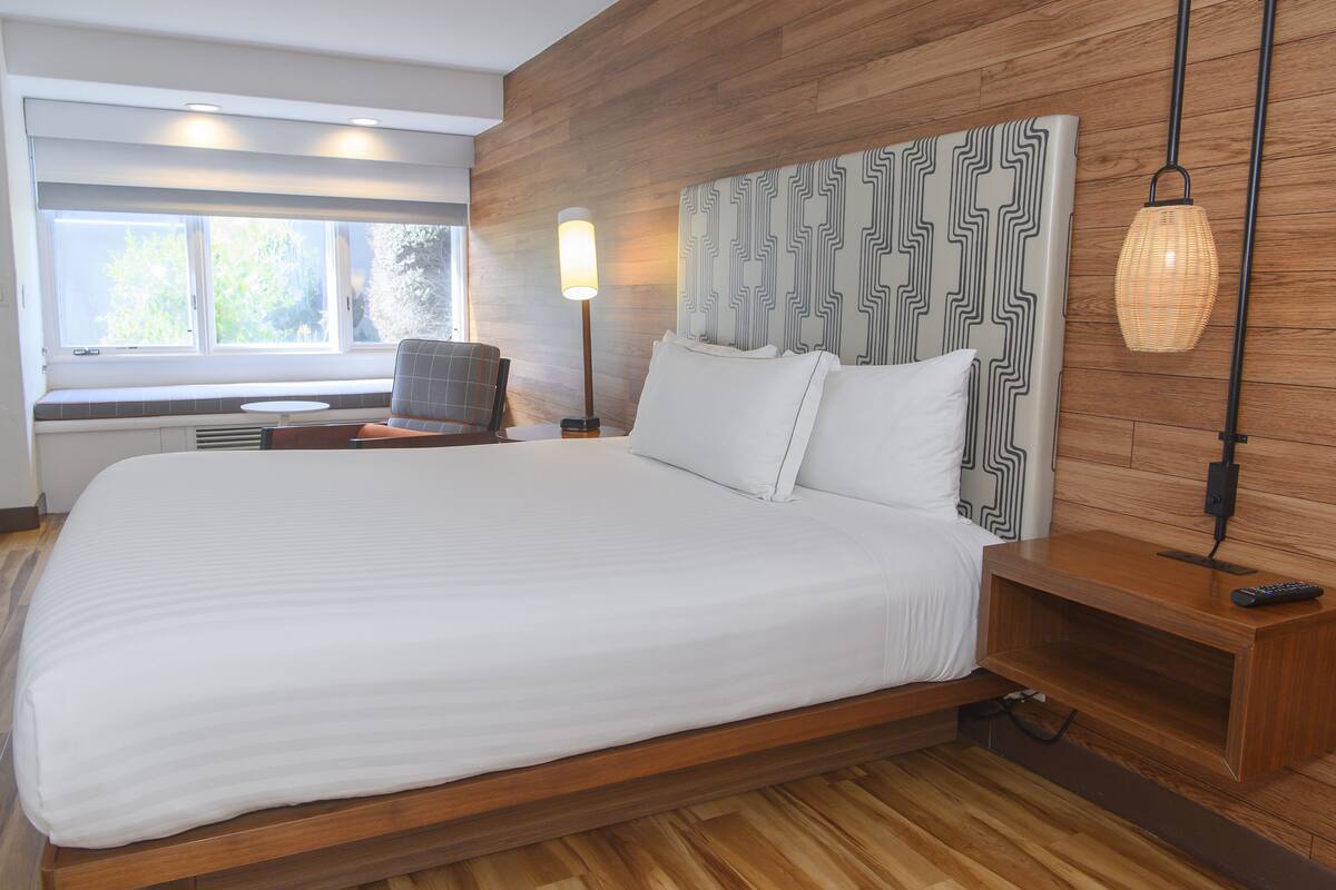 A modern bedroom with a large bed, wooden headboard, bedside tables, and a window with a view.