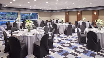 A banquet hall with round tables, black chairs, and white tablecloths.
