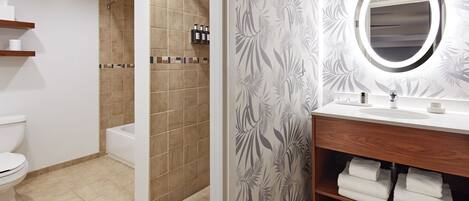 A bathroom with a toilet, a shower, a sink with a mirror, and a shelf with towels.