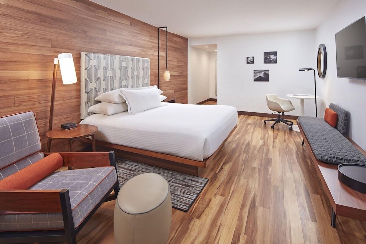 A modern hotel room with a large bed, a sofa, a desk, and a chair.