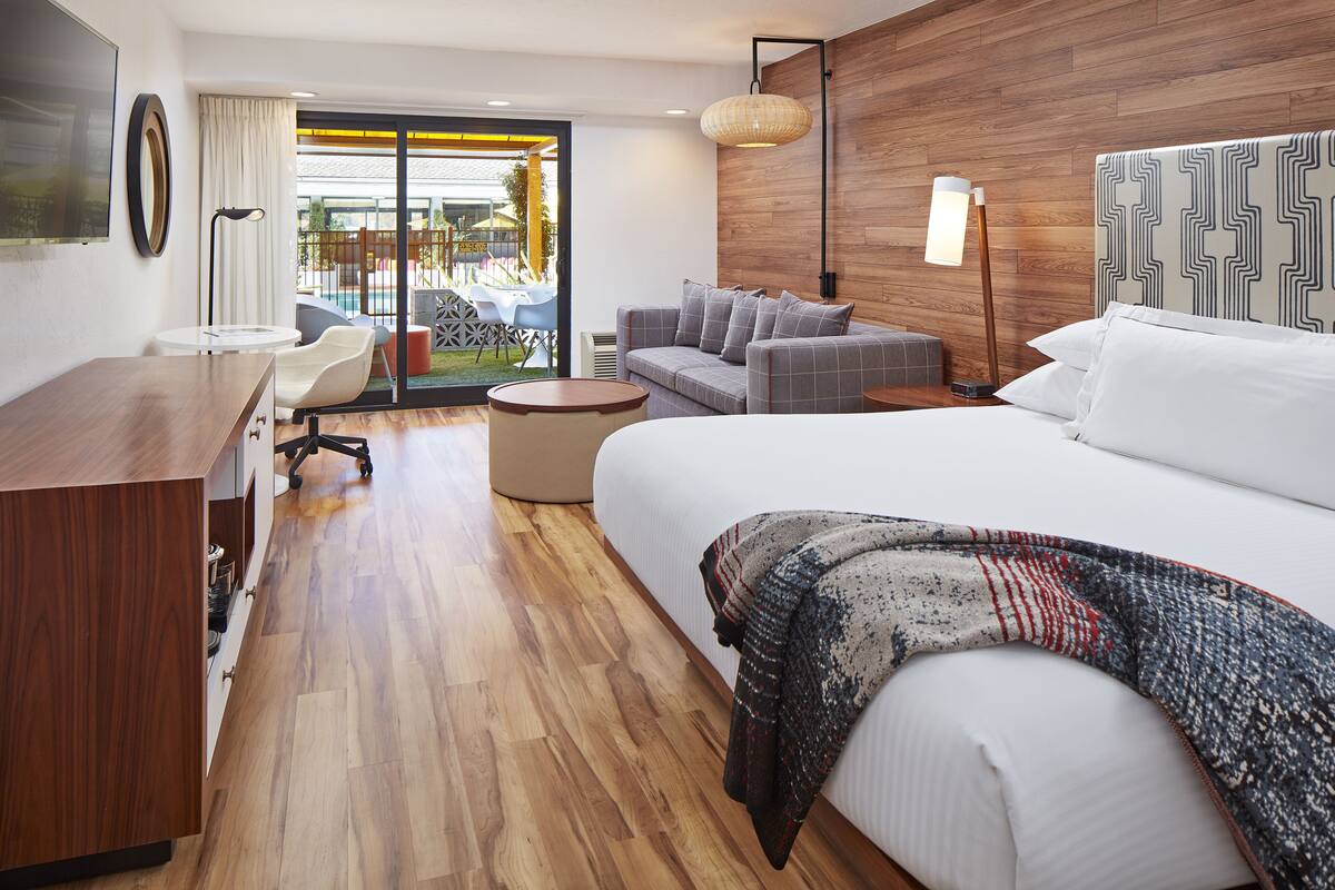 A hotel room with a large bed, a sofa, a desk, and a view of the outdoor area.