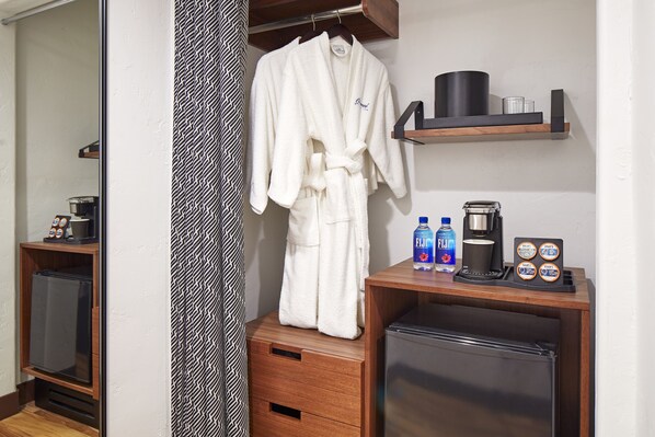 A hotel room with a wooden cabinet, a minibar, a coffee machine, and a robe hanging on a rack.