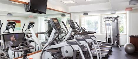 Un gimnasio con cintas de correr, elípticas, una bicicleta estática, una máquina de remo y una pelota grande de ejercicio.