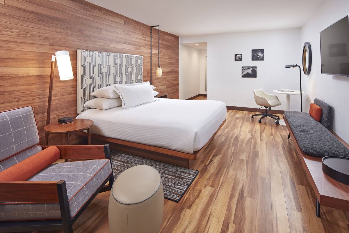 A modern hotel room with a large bed, a sofa, a desk, and a chair.