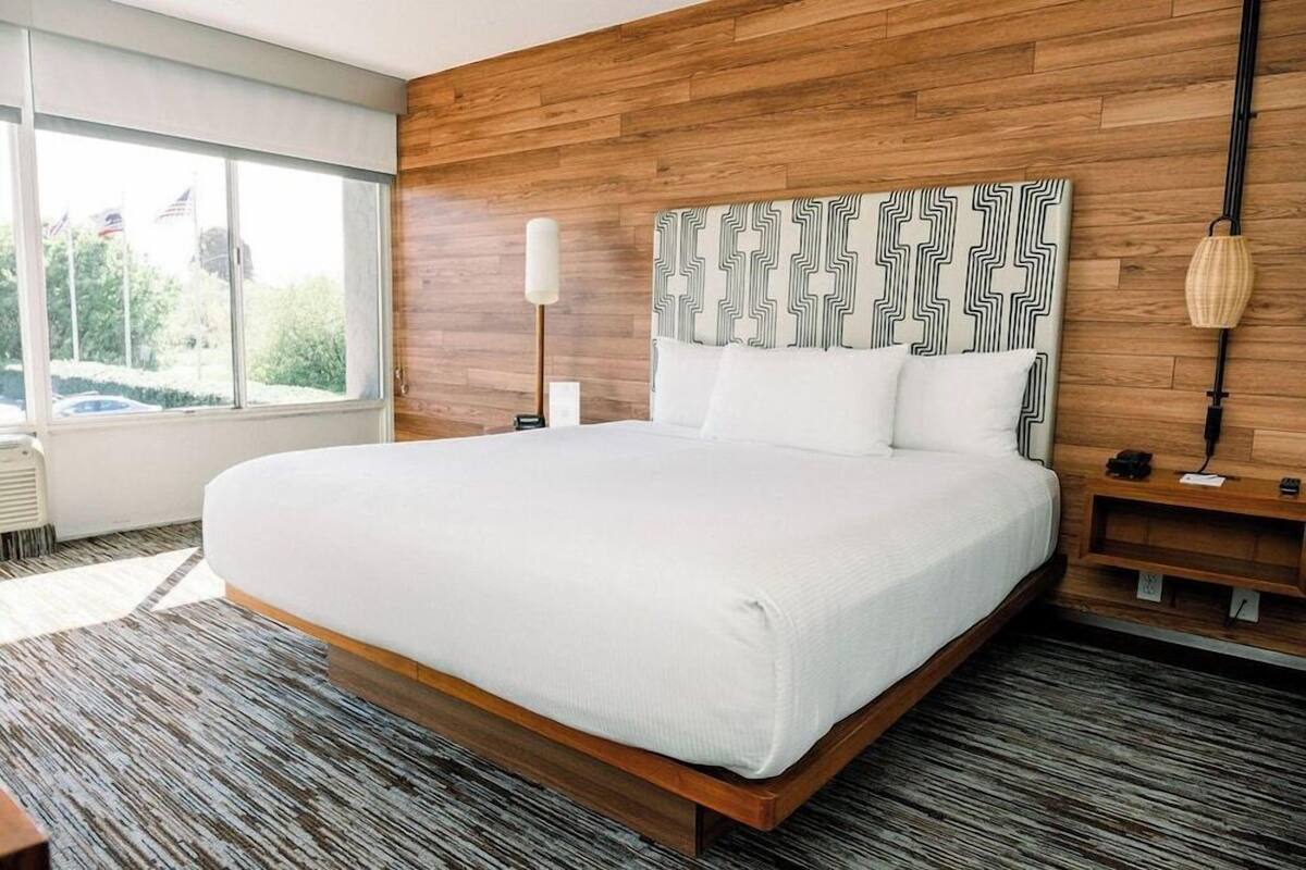 A modern hotel room with a large bed, wooden headboard, and a view of the outdoors.