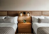 A hotel room with two beds, a wooden nightstand, and a woven headboard.