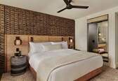 A bedroom with a large bed, a ceiling fan, a woven headboard, and a mirror with a towel rack.