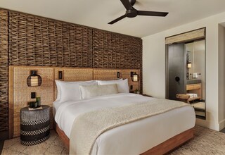 A bedroom with a large bed, a ceiling fan, a woven headboard, and a mirror with a towel rack.