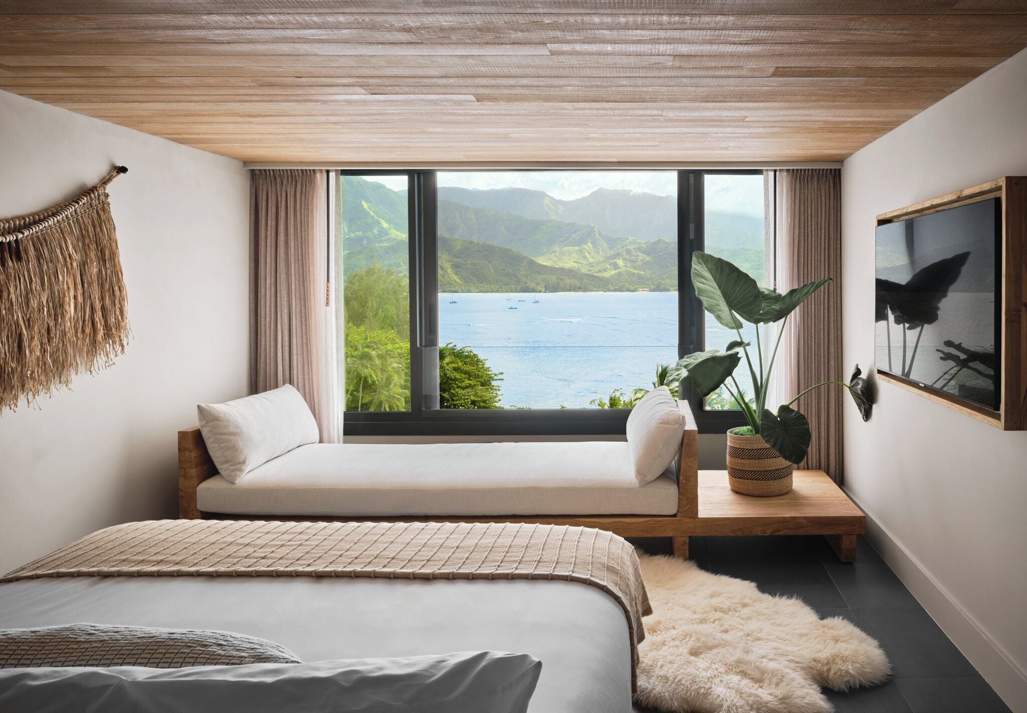 Un dormitorio con un ventanal grande, una cama, un sofá, una planta y un cuadro enmarcado.