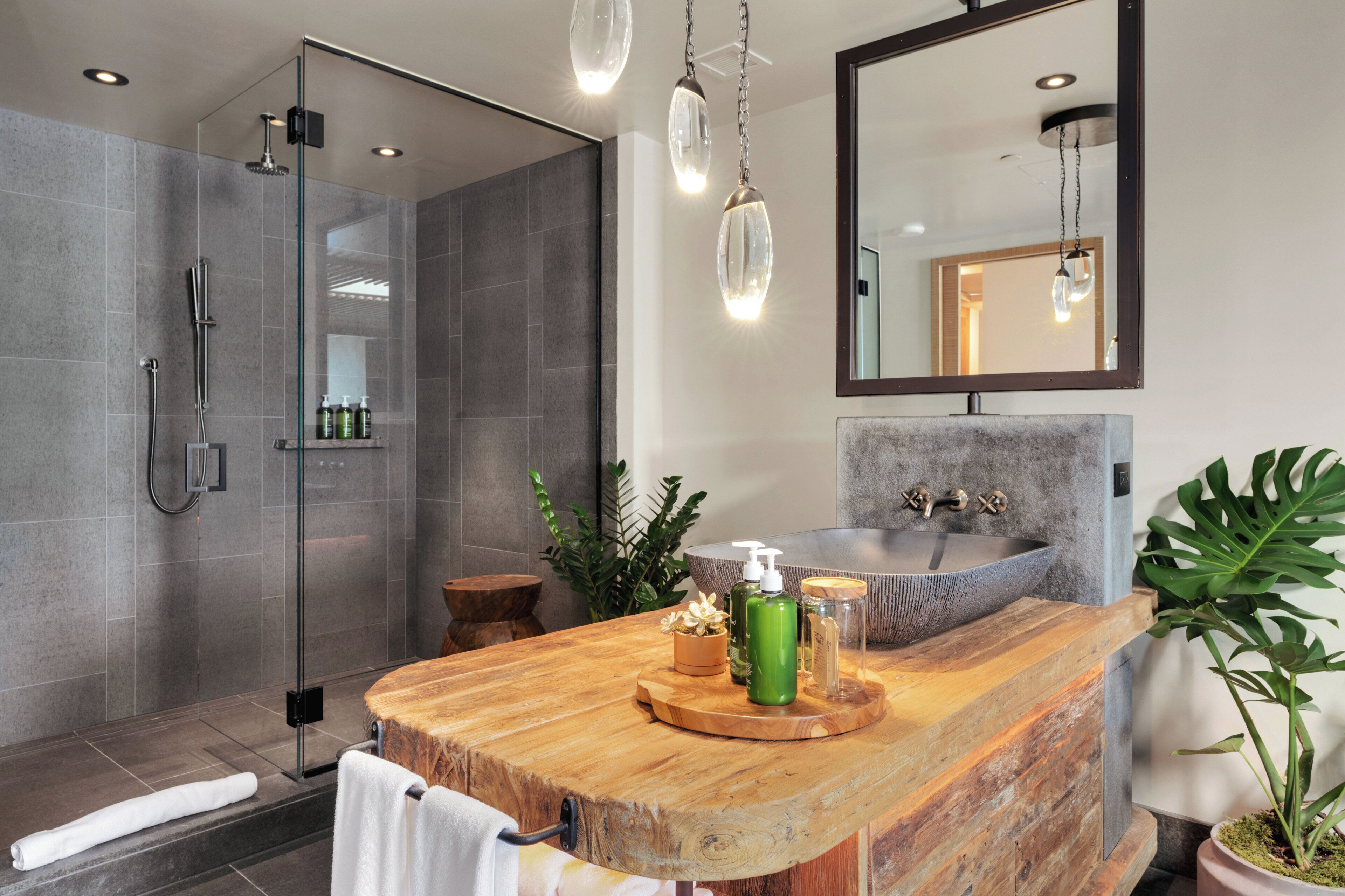 A modern bathroom with a glass shower enclosure, a wooden vanity with a stone sink, and a large mirror above the vanity.