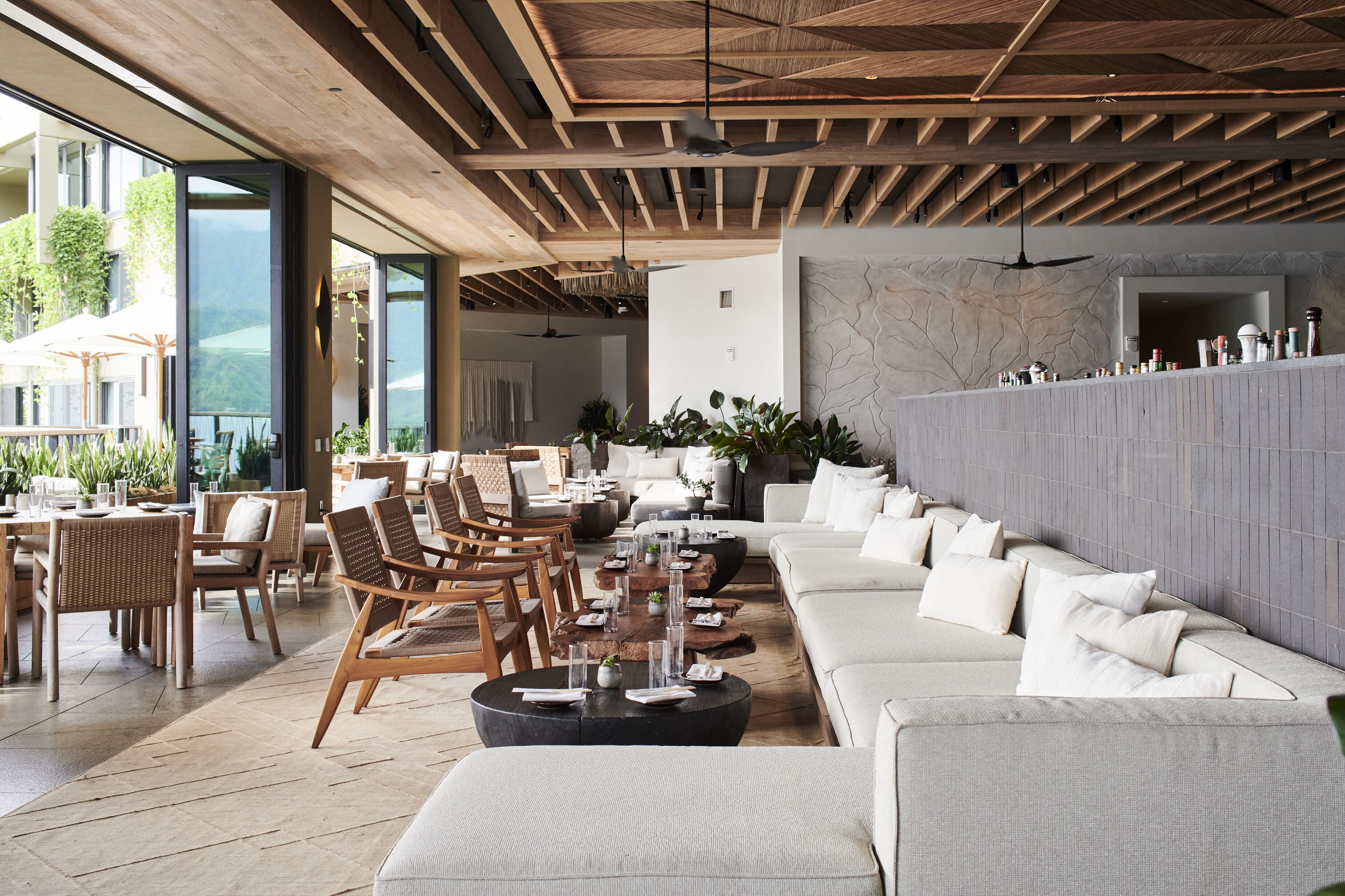 A modern lounge area with a long sofa, wooden chairs, and a coffee table.